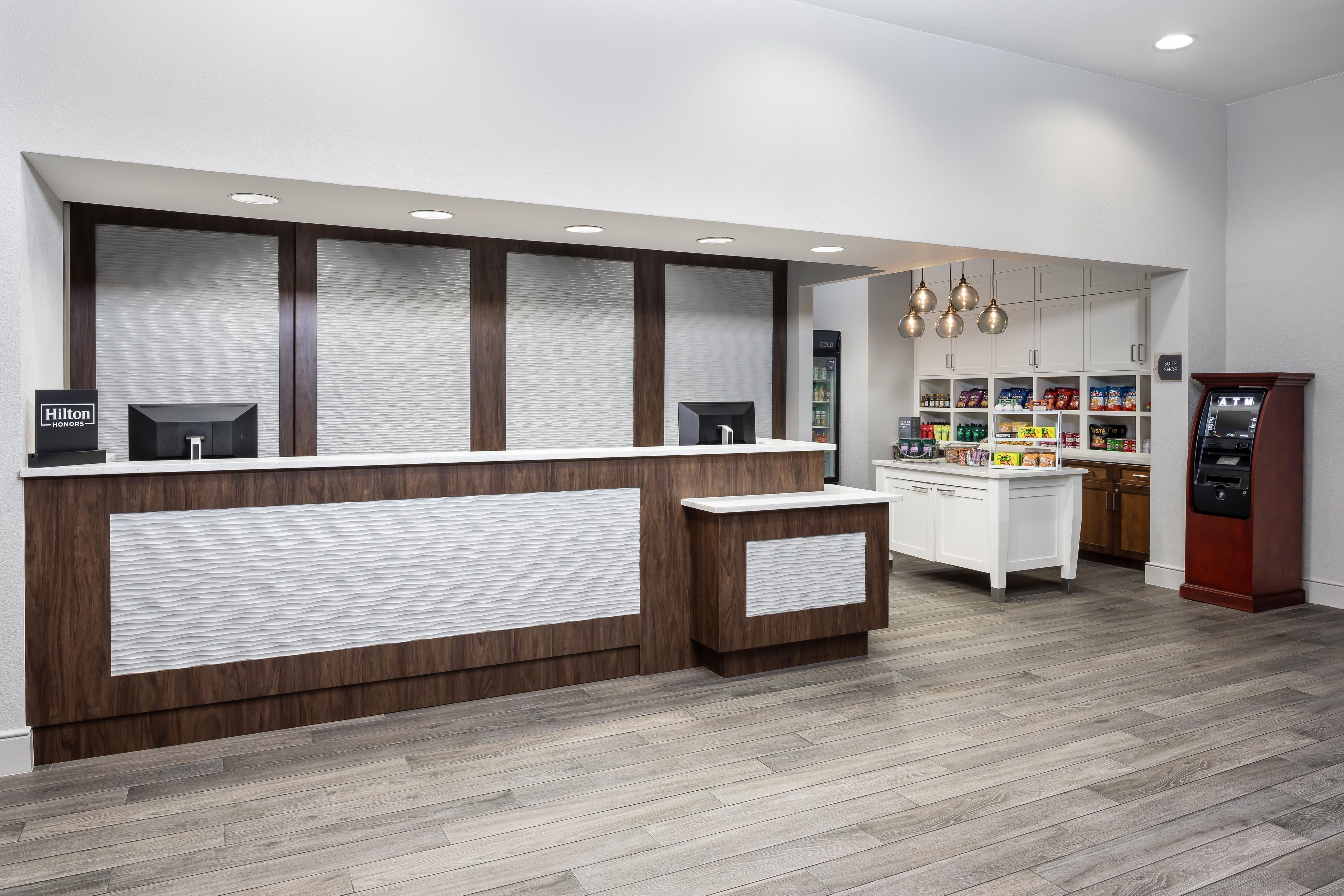 A hotel reception area with a wooden reception desk, a minibar, and a self-service beverage machine.