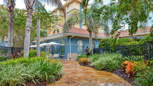A courtyard with a paved walkway, palm trees, and a building with a tiled roof and arched windows. - Homewood Suites by Hilton Lake Buena Vista - Orlando (Orlando)