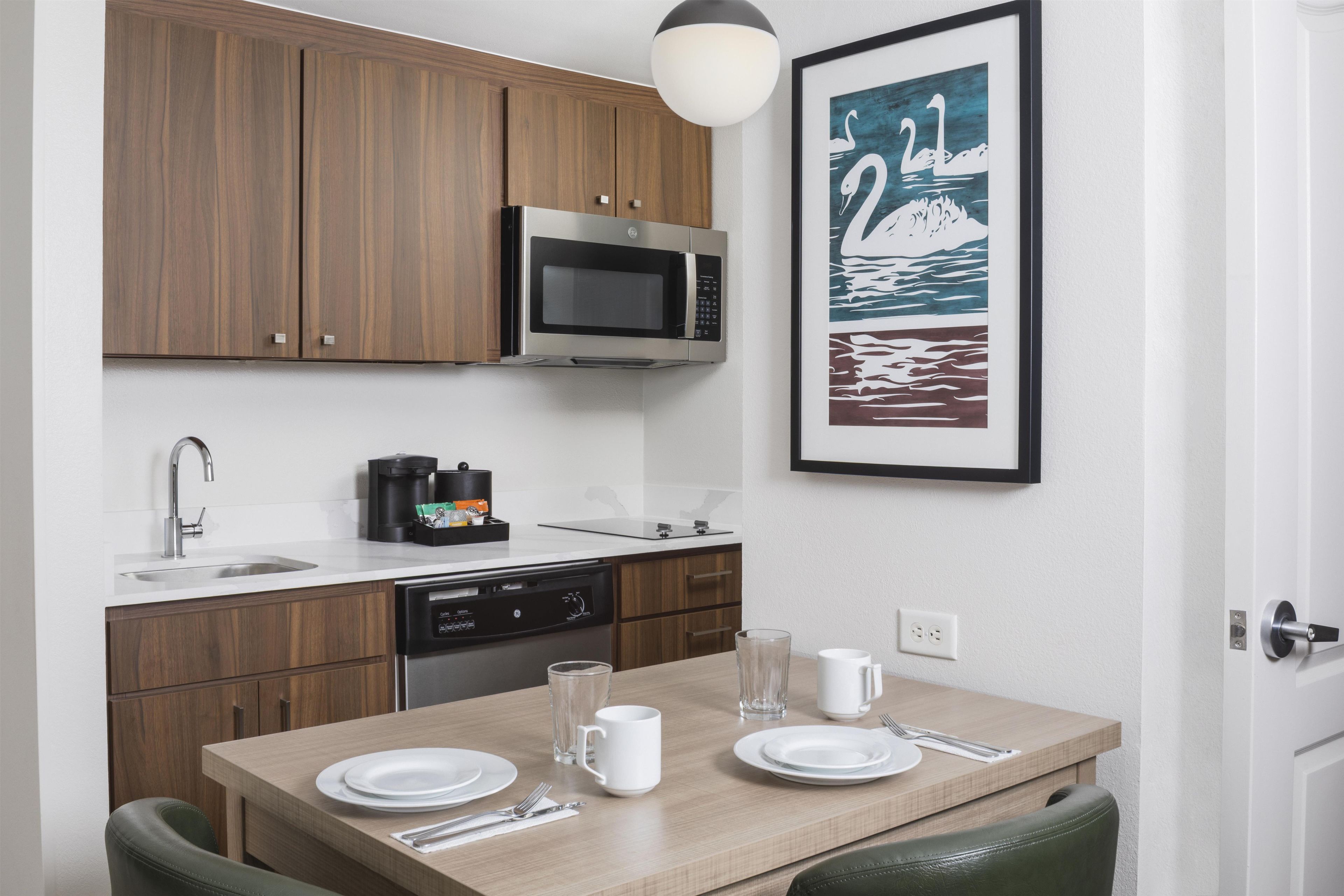 A compact kitchen with wooden cabinets, a microwave, a coffee maker, and a dining table set for two.