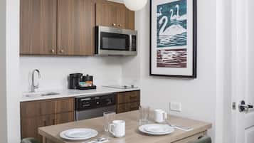 A compact kitchen with wooden cabinets, a microwave, a coffee maker, and a dining table set for two.