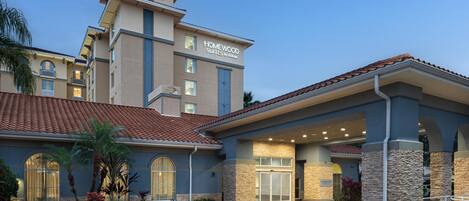 A hotel with a modern design, featuring a prominent entrance with a covered walkway and a sign indicating it is a Homewood Suites by Hilton.