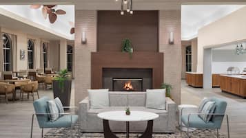 A modern living room with a fireplace, seating area, and a kitchen in the background.