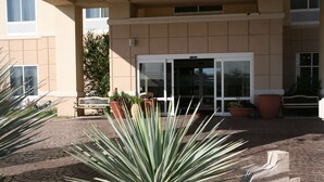 Une entrée d’immeuble avec une allée pavée, des plantes en pot et un banc.