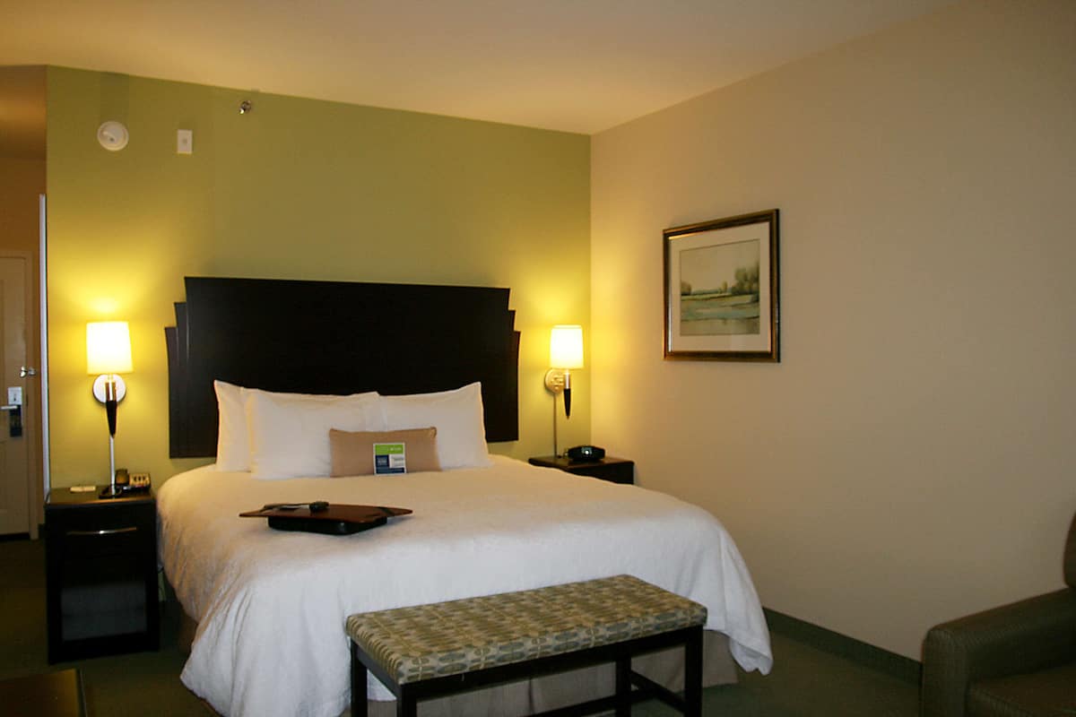 A hotel room with a large bed, two bedside tables with lamps, a bench, and a framed picture on the wall.