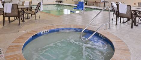 Zona de piscina de hotel con un jacuzzi, sillas de descanso y mesas.