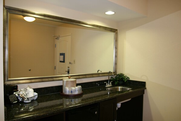 A bathroom with a large mirror, a sink, a towel dispenser, and a tray with toiletries.