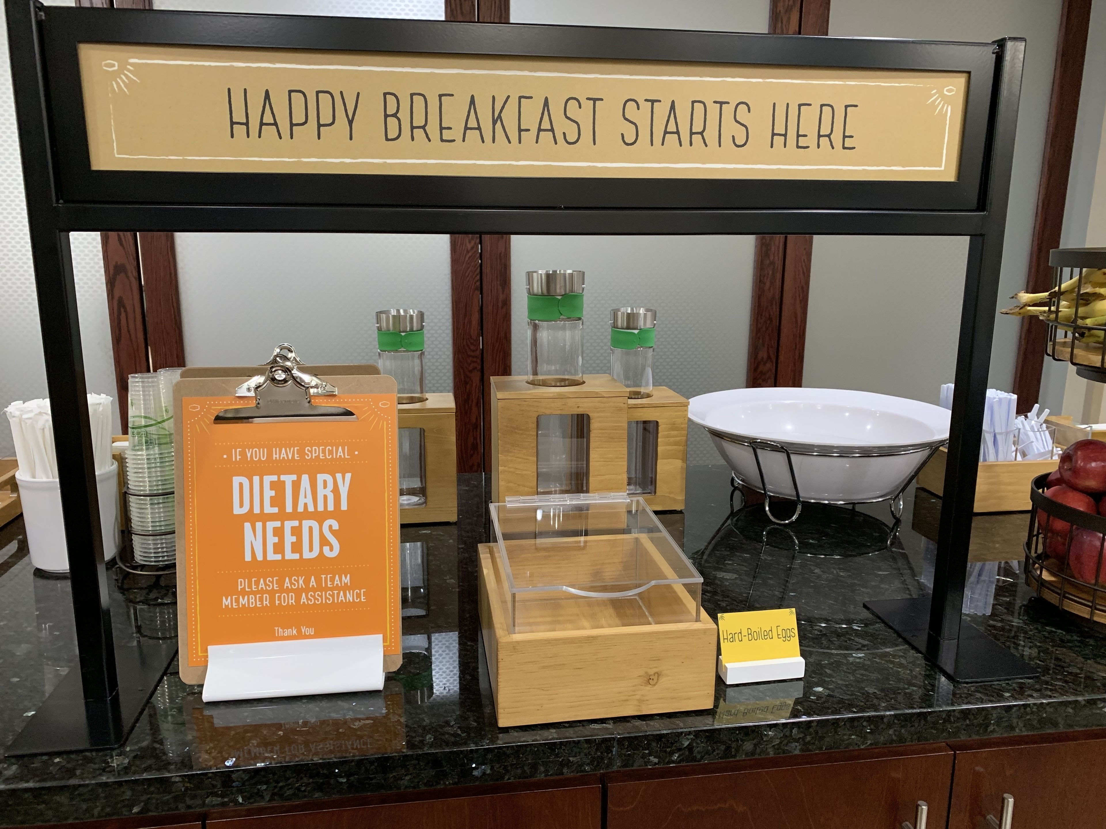 A breakfast area with a sign that reads "HAPPY BREAKFAST STARTS HERE" and a sign for dietary needs.