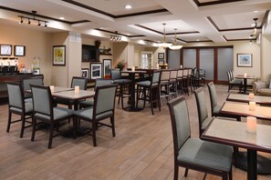 A restaurant with multiple dining tables and chairs, a bar area, and framed pictures on the walls.