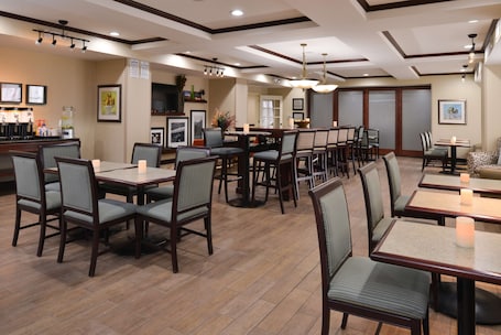 A restaurant with multiple dining tables and chairs, a bar area, and framed pictures on the walls.
