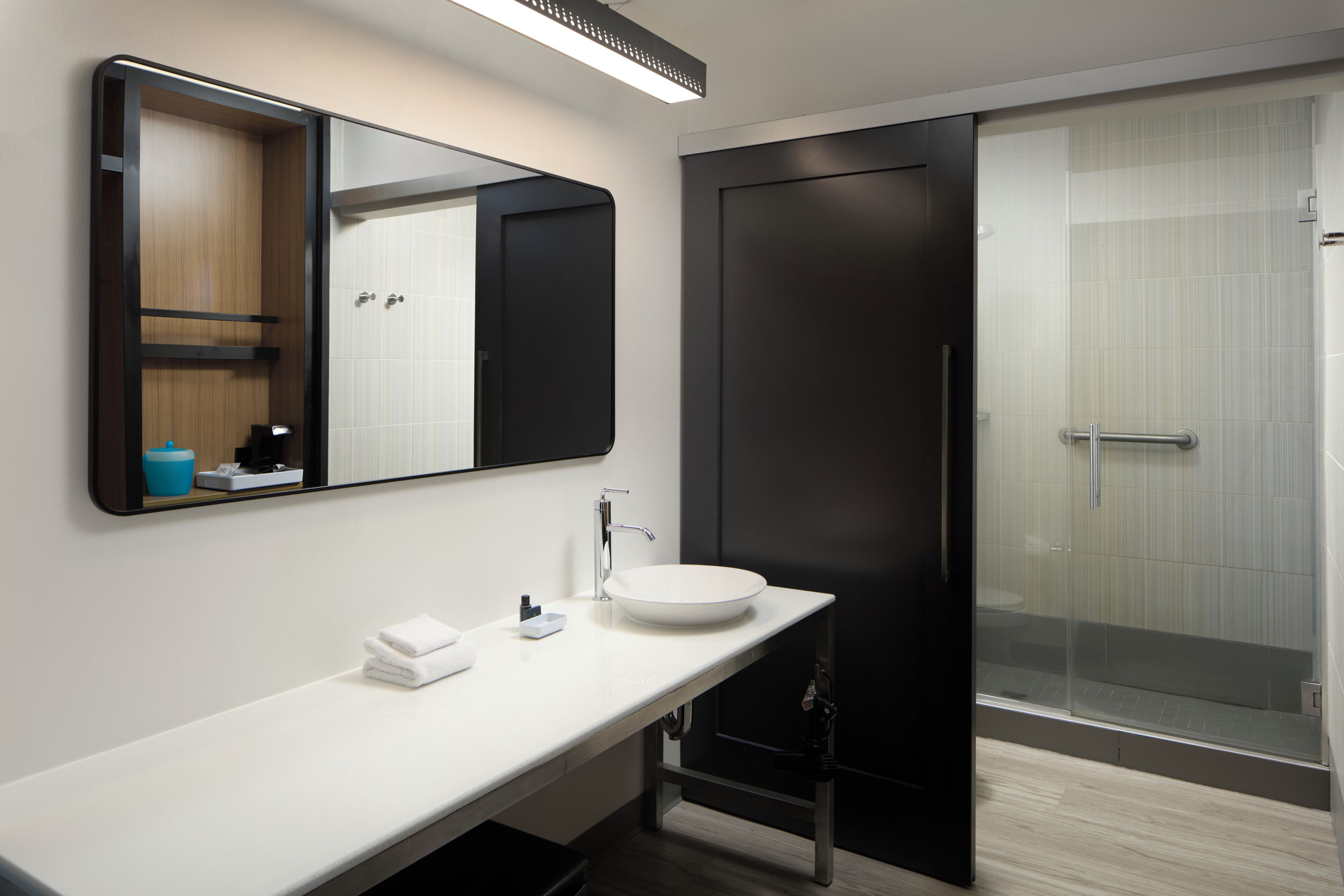 A modern bathroom with a white sink, a mirror, a towel rack, and a shower area.