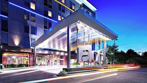 A modern hotel with a prominent entrance, large windows, and a clear sky. - Aloft by Marriott Arundel Mills BWI Airport (Hanover)