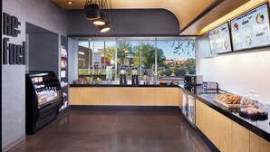 A modern cafe interior with a self-service beverage station, wooden counter, and menu boards. - Aloft by Marriott Tempe (Tempe)
