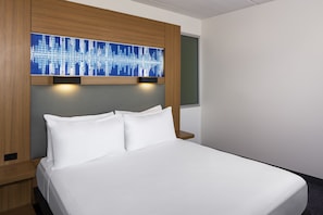 A modern hotel room with a large bed, wooden headboard, and a cityscape artwork above the bed. - Aloft by Marriott Tempe (Tempe)
