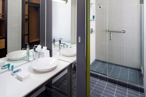 A modern bathroom with two sinks, a mirror, and a glass-enclosed shower. - Aloft by Marriott Tempe (Tempe)