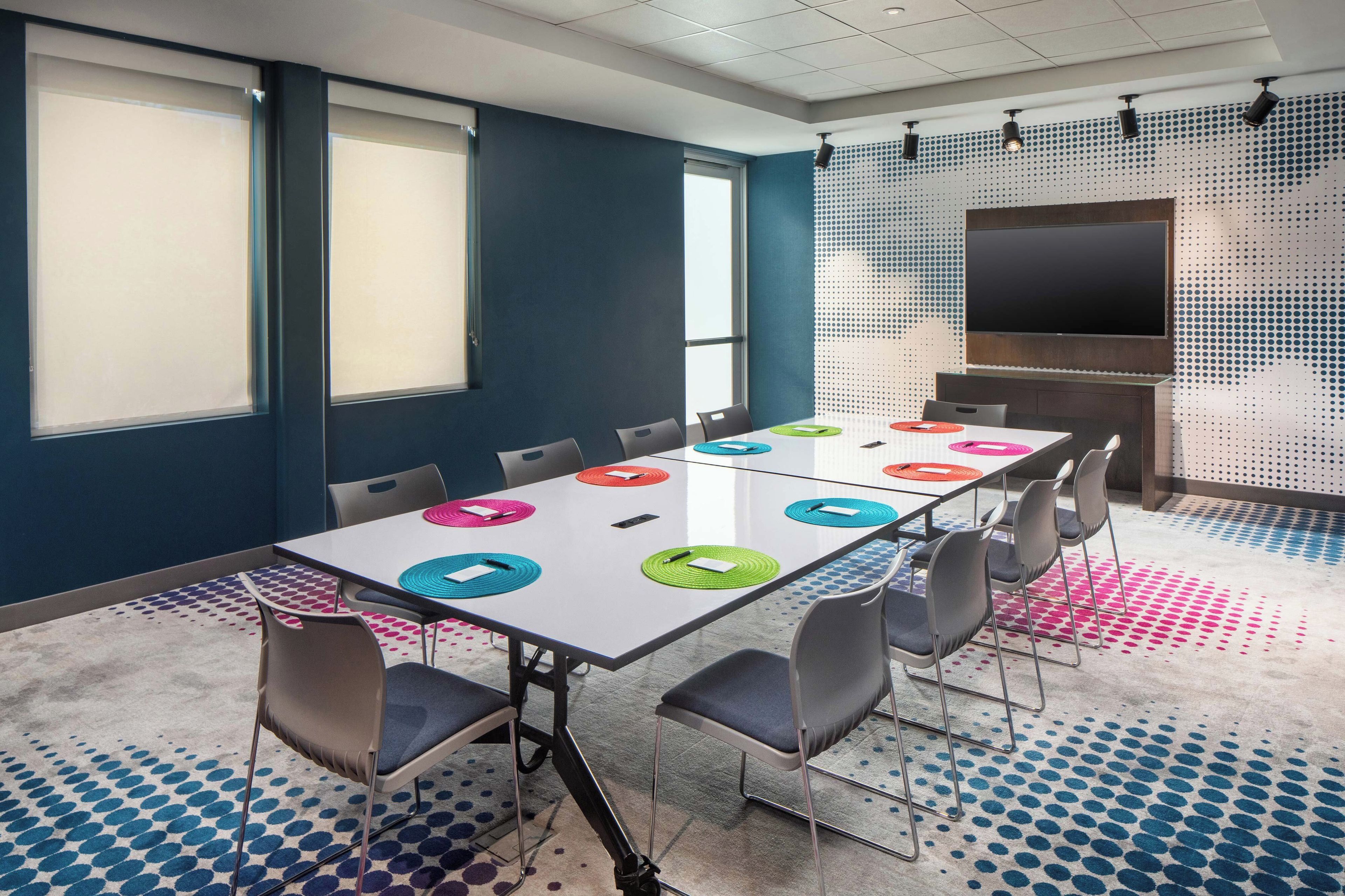Sala de conferências com uma mesa comprida, cadeiras e uma tela grande.