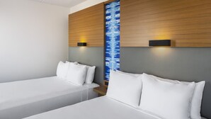 A hotel room with two single beds, a wooden headboard, a wall-mounted light, and a blue patterned wall. - Aloft by Marriott Tempe (Tempe)
