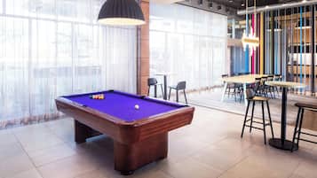 A pool table with balls, a bar area with stools, and large windows with sheer curtains.