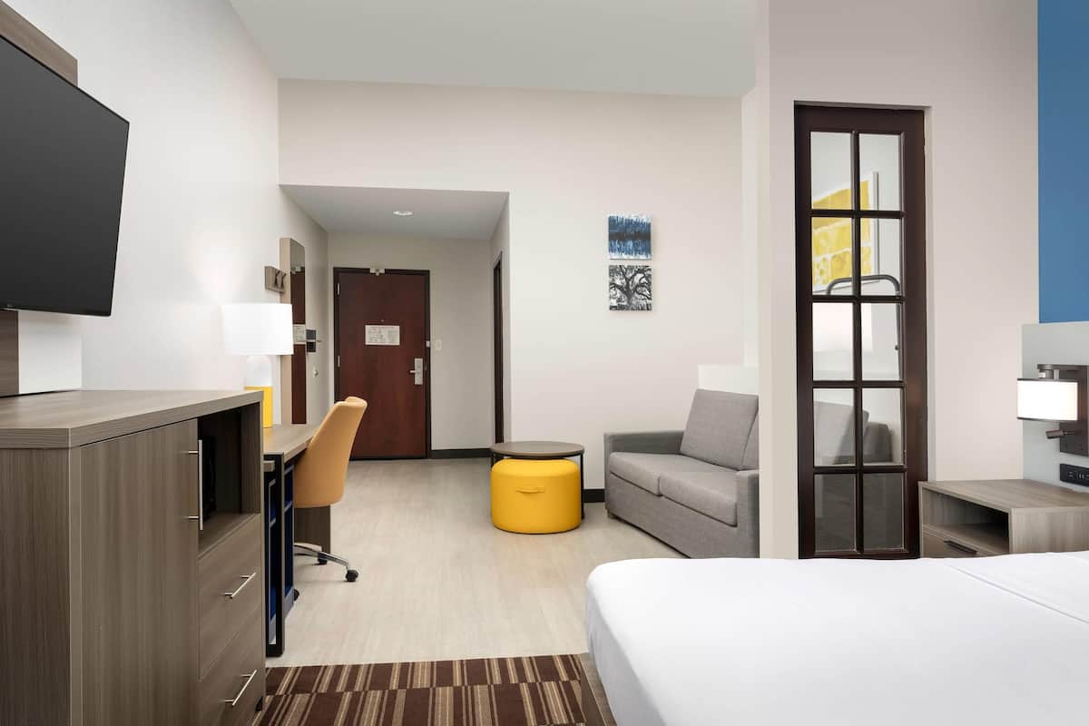 A hotel room with a bed, a desk, a chair, a sofa, a small round table, and a TV.