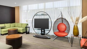A modern living room with a sectional sofa, a round coffee table, a hanging chair, and a flat-screen TV on a glass stand.