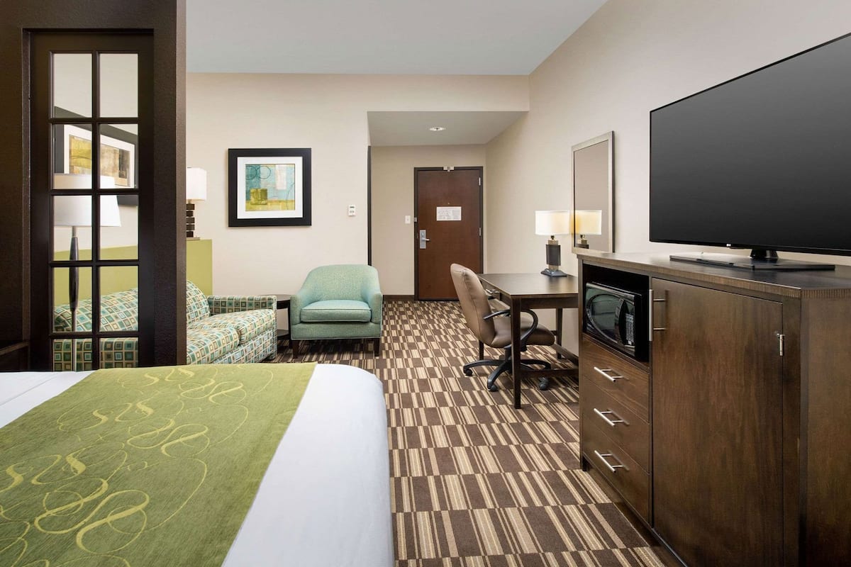 A hotel room with a bed, a desk with a TV, a chair, and a door.