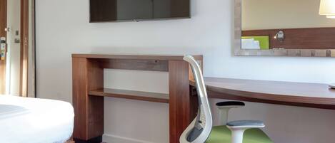 Une chambre d’hôtel comprenant un lit, un bureau avec une chaise, une télévision et un miroir.