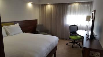 Hotellihuone, jossa on sänky, työpöytä, tietokone, tuoli ja lamppu.