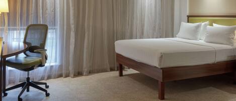 Habitación de hotel con cama, escritorio con silla y ventana con cortinas.