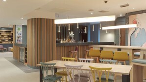 A modern bar area with a wooden accent wall, multiple seating options, and a bar counter. - Hampton by Hilton Corby/Kettering (Corby)