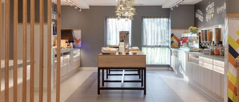 A modern kitchen with a central island, large windows, and a decorative chandelier.