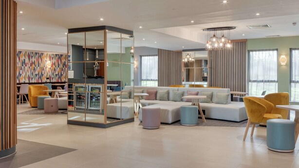 A modern lounge area with seating, a bar, and a large window providing natural light. - Hampton by Hilton Corby/Kettering (Corby)