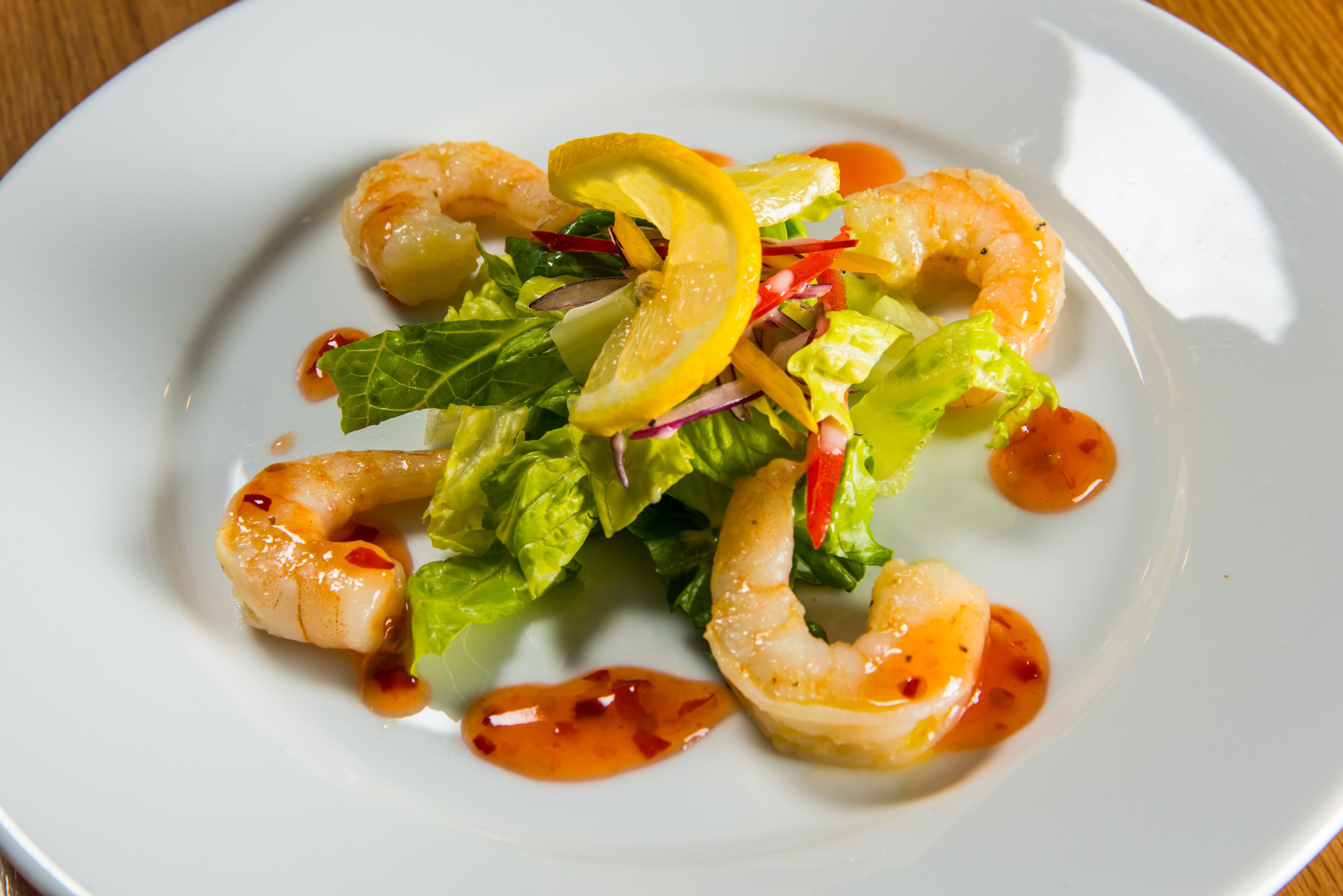 A plate of shrimp and salad with lemon slices and sauce.
