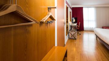 Une chambre d’hôtel avec une armoire en bois, un banc, un bureau avec une chaise, une télévision et un lit.