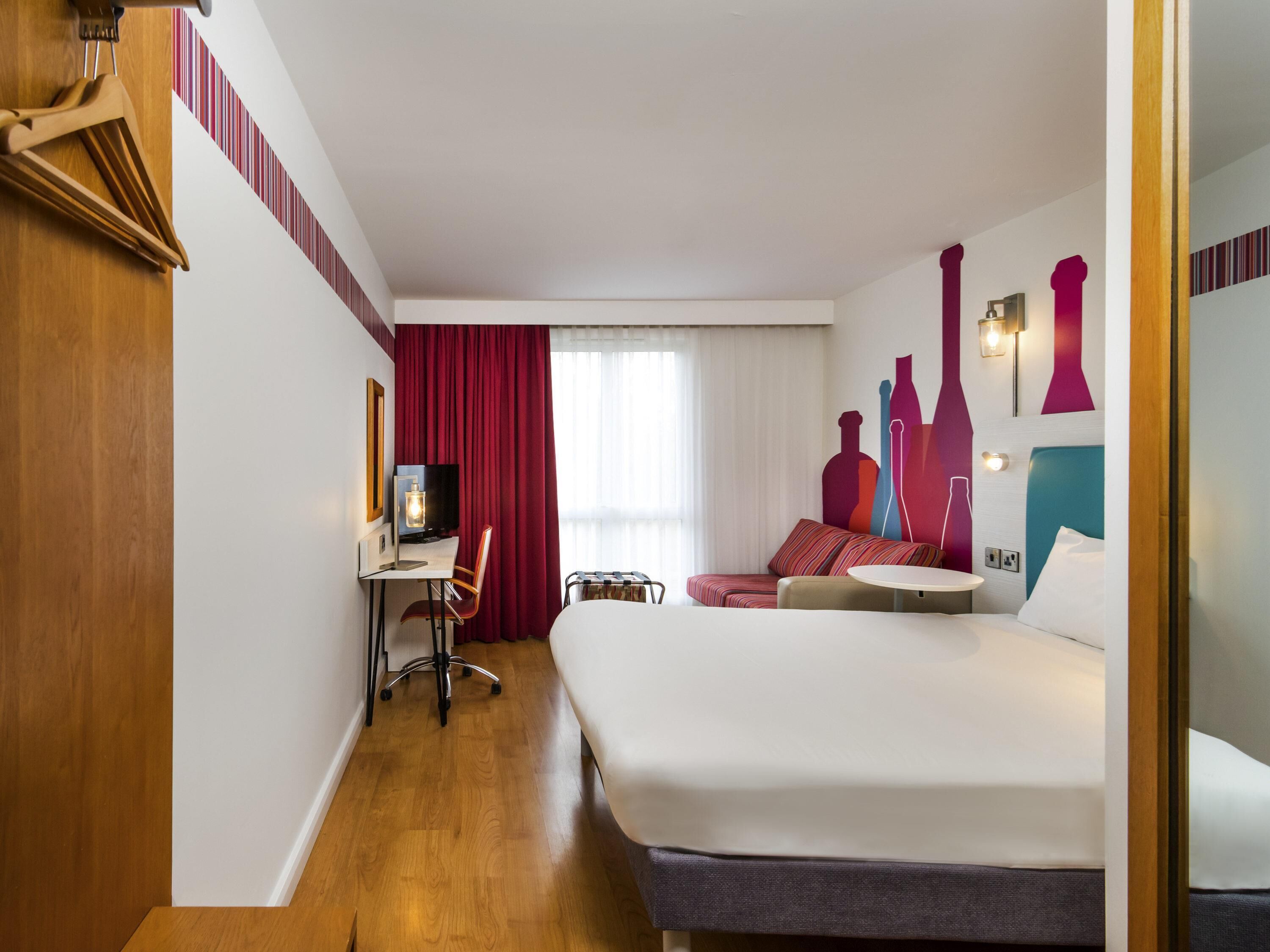 A hotel room with a bed, a desk with a chair, a TV, and a sofa.