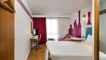 A hotel room with a bed, a desk with a chair, a TV, and a sofa.