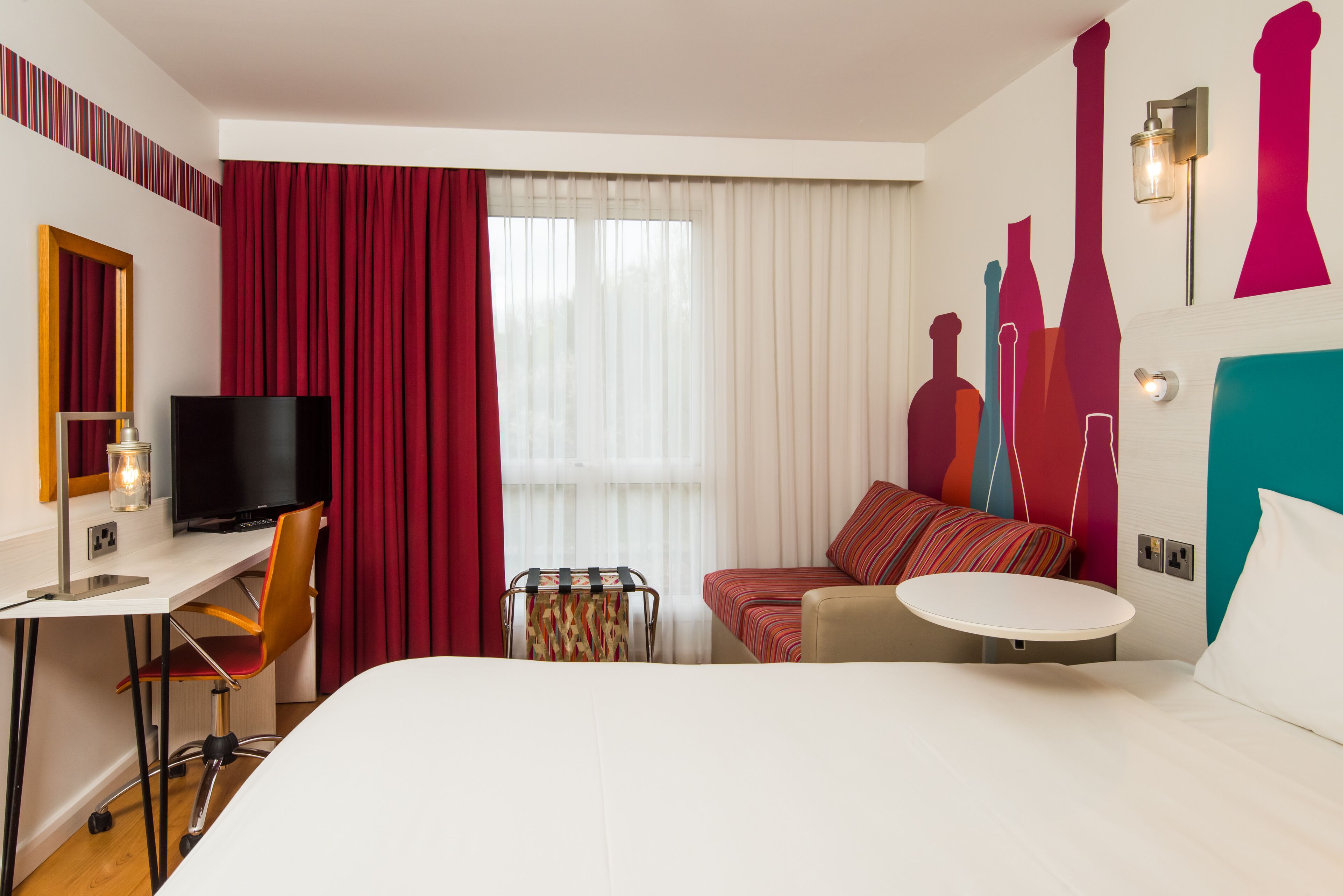Et hotelværelse med en seng, et skrivebord med tv, en stol, et lille bord og en sofa.