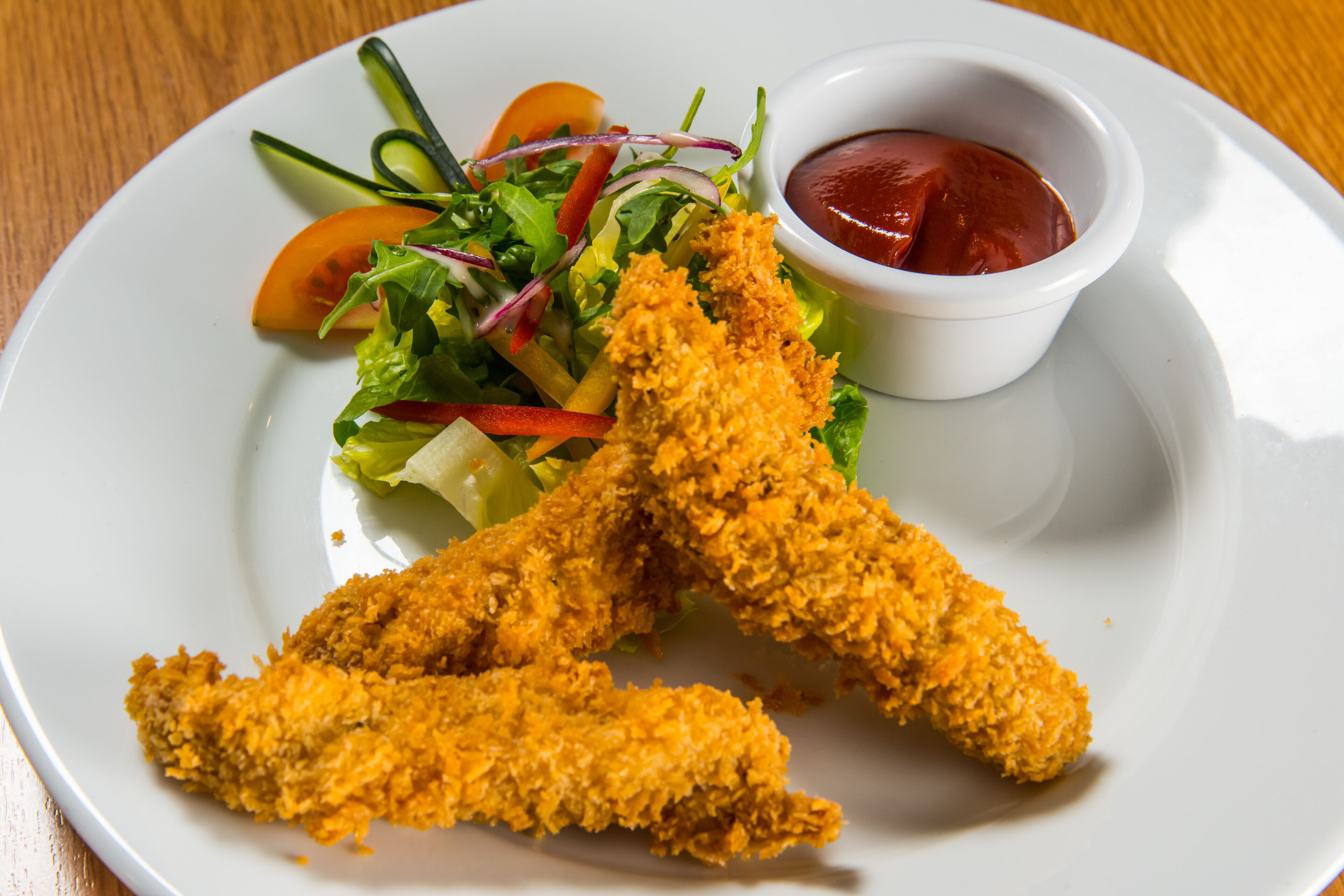 A plate with breaded chicken tenders, a side salad, and a small bowl of ketchup.