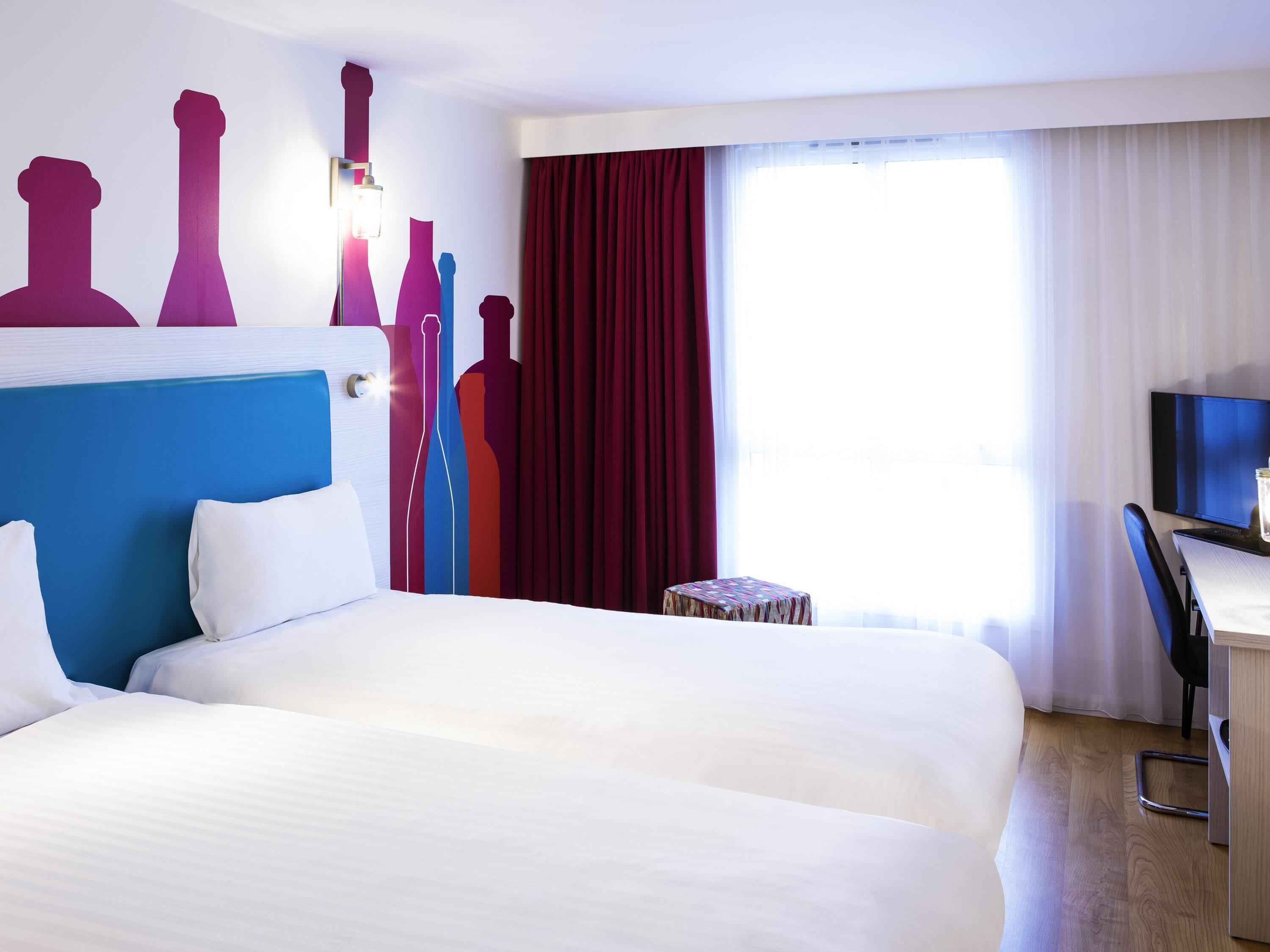 A hotel room with a large bed, a desk with a chair, a television, and a window with curtains.