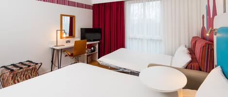 Une chambre d’hôtel comprenant un lit, un bureau avec une télévision, une chaise, une petite table et une fenêtre avec des rideaux.