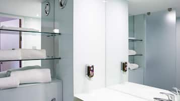 Un baño moderno con un espejo grande, estantes de vidrio con toallas y un lavabo blanco.