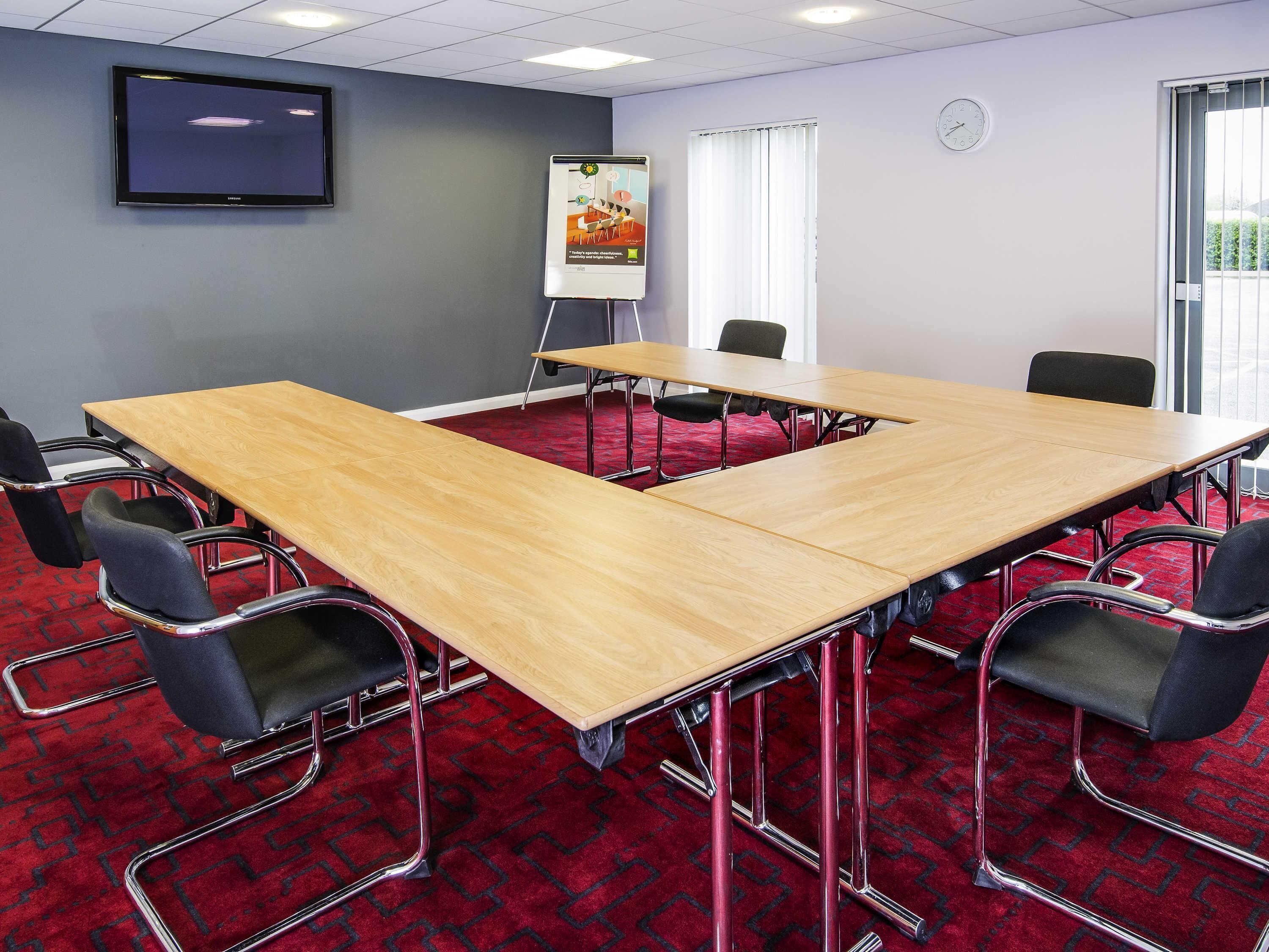 A conference room with a large table, chairs, a whiteboard, a clock, and a TV on the wall.