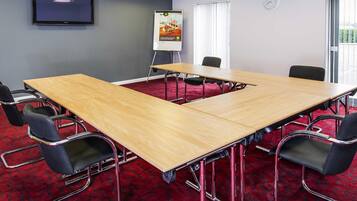 A conference room with a large table, chairs, a whiteboard, a clock, and a TV on the wall.
