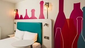 Hotelkamer met een blauwgroen hoofdeinde, witte beddengoed en een wand met abstracte kunst.