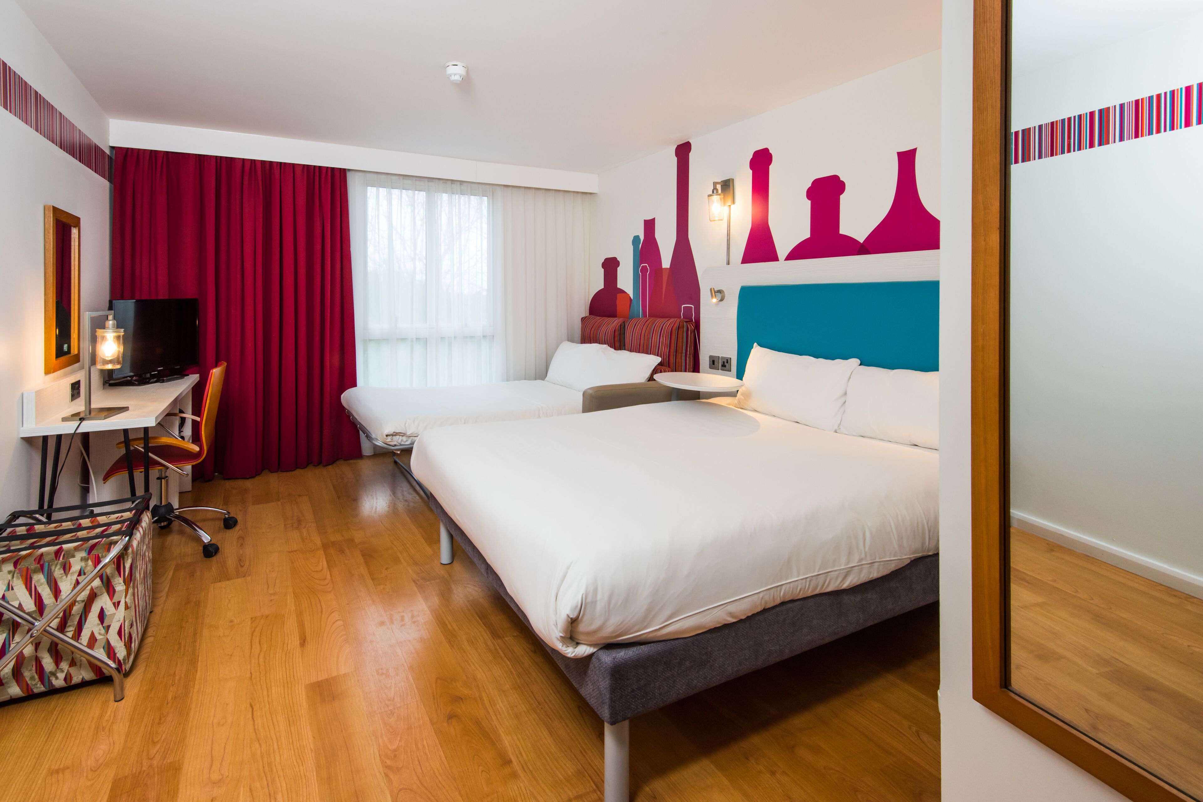 A hotel room with a bed, a desk, a chair, a TV, and a window with curtains.