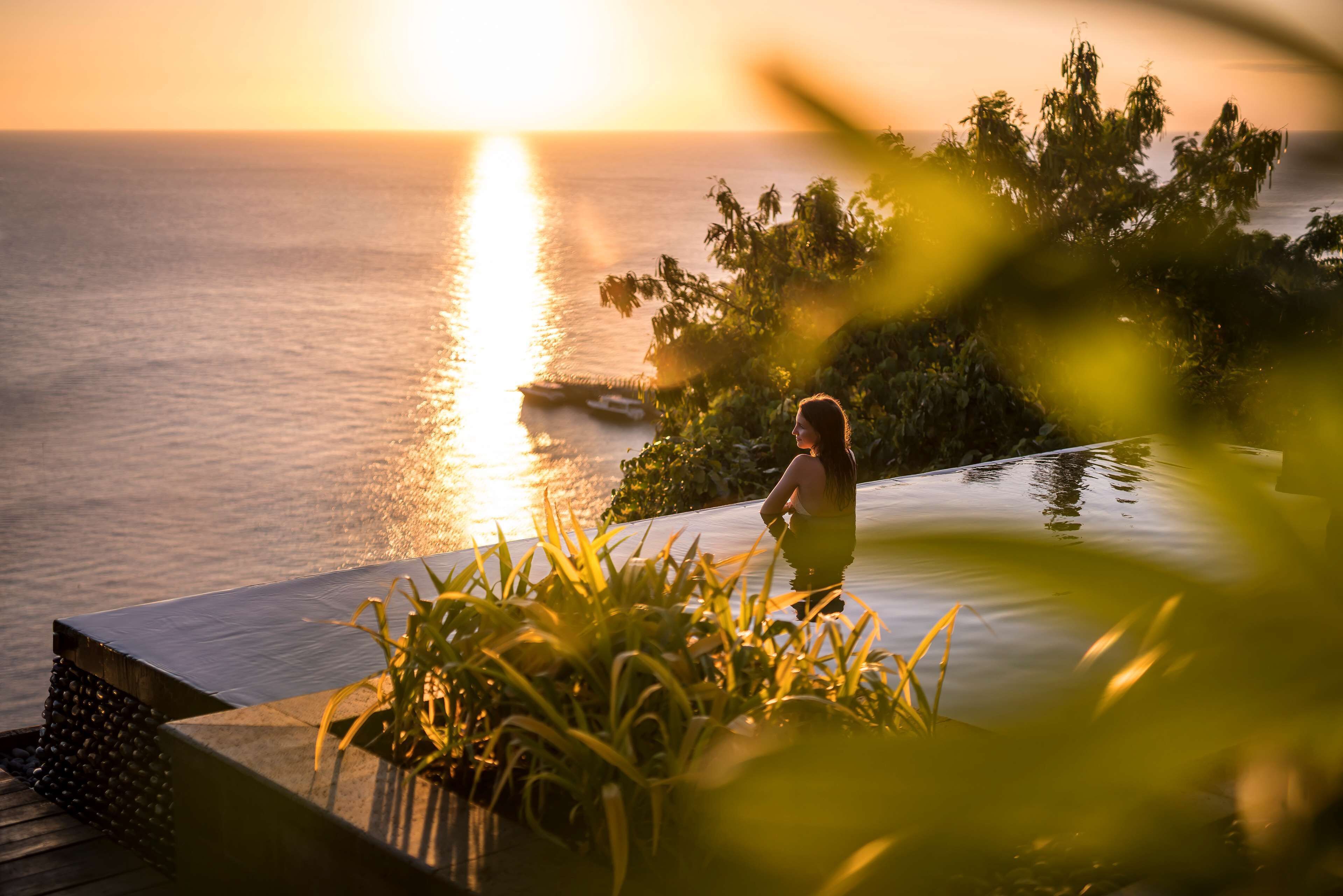 A person sitting by a pool at sunset with a view of the ocean.