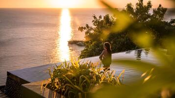 A person sitting by a pool at sunset with a view of the ocean.