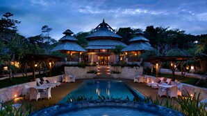 A resort with a swimming pool, outdoor seating, and a traditional building with multiple roofs.