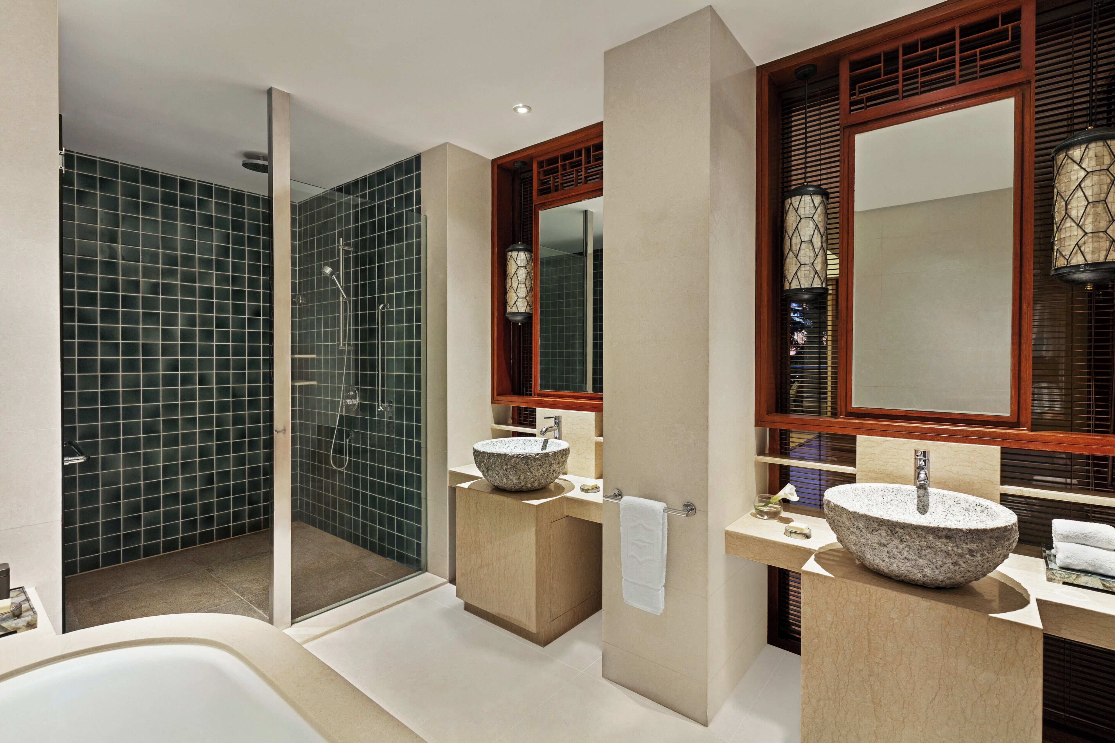 Un baño moderno con ducha envuelta en vidrio, dos lavamanos de piedra y un espejo grande.