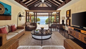A spacious living room with a large TV, comfortable seating, and a view of the ocean.