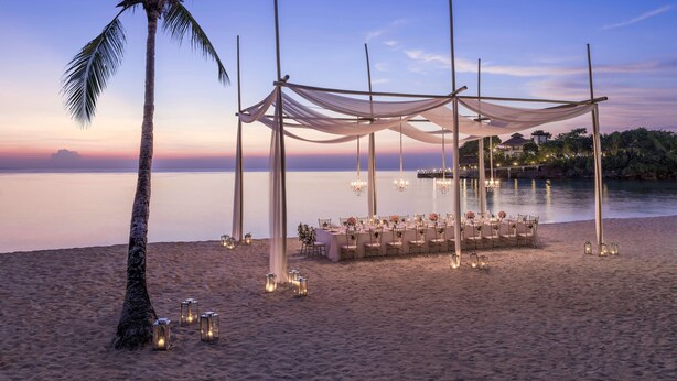 Une cérémonie de mariage organisée sur la plage, avec un auvent, des tables, des chaises et des lanternes.