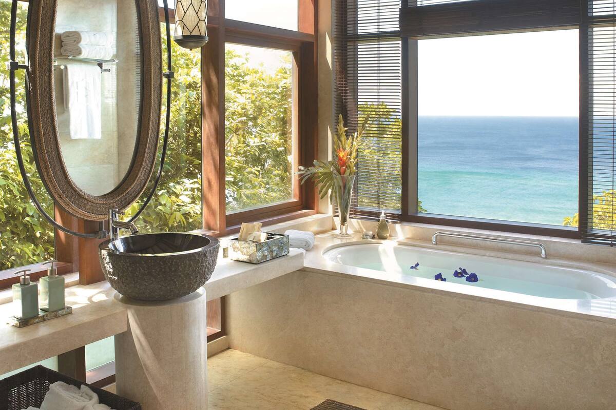 Ein Badezimmer mit einer großzügigen Badewanne, einem runden Spiegel und Blick auf den Ozean.